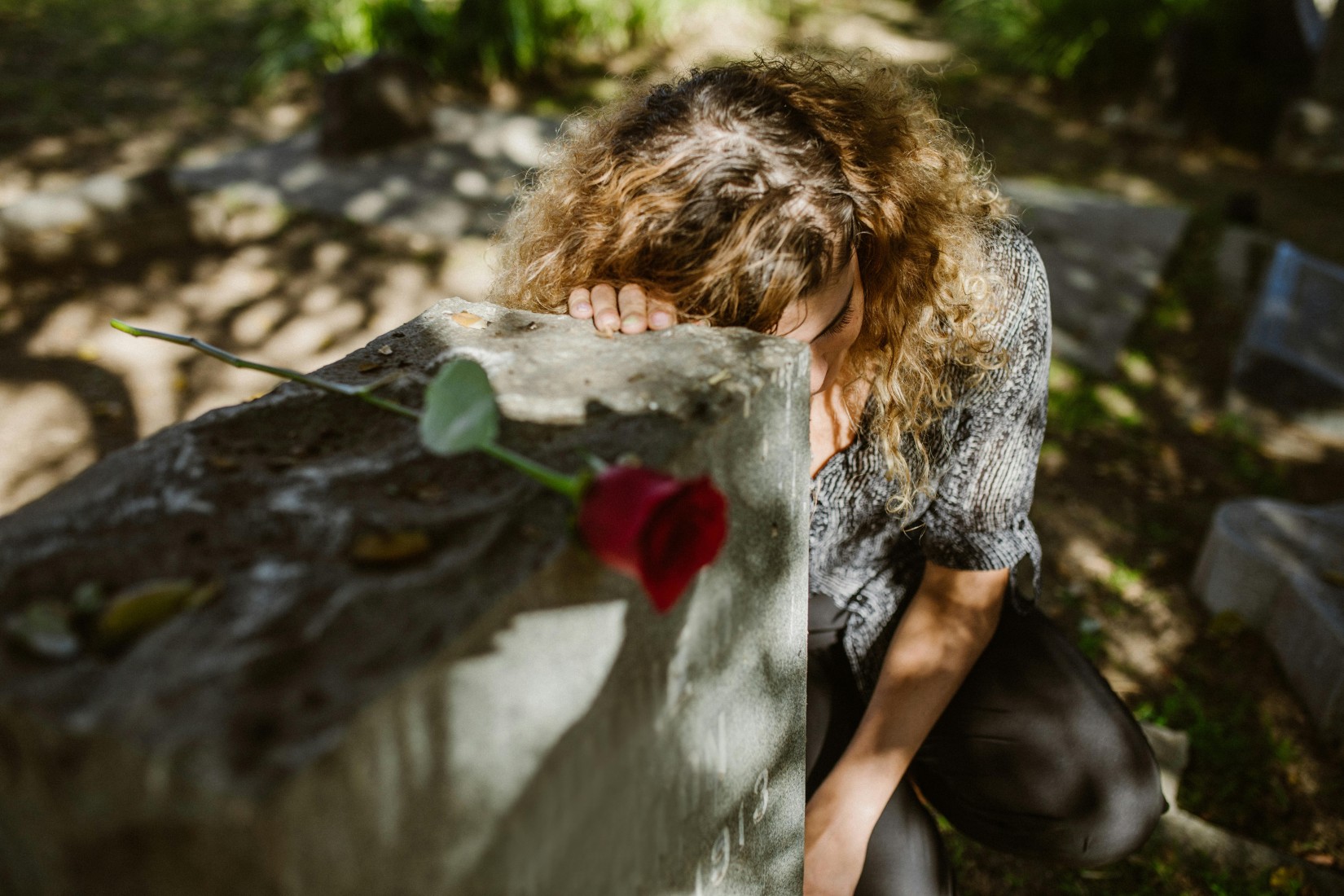 Woman mourning at a gravesite with a red rose, symbolizing grief, loss, and remembrance